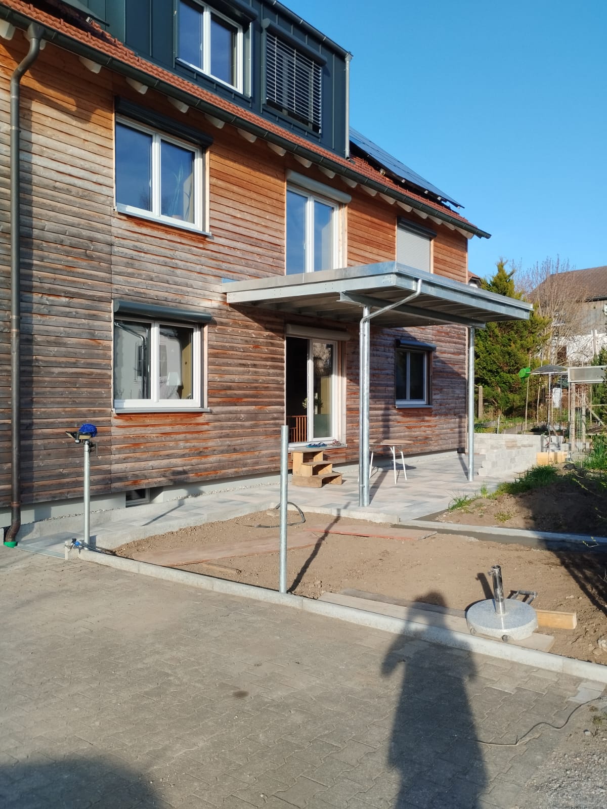 Außenbereich mit Holzfassade, Terrassenüberdachung und neuer Pflasterung